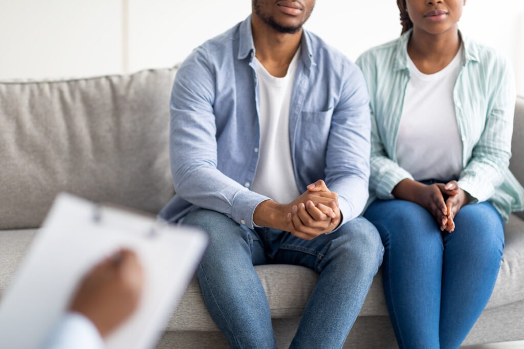 Cropped view of young black married couple on consultation with psychologist, undergoing family therapy at clinic. Unrecognizable spouses having appointment with psychotherapist, closeup